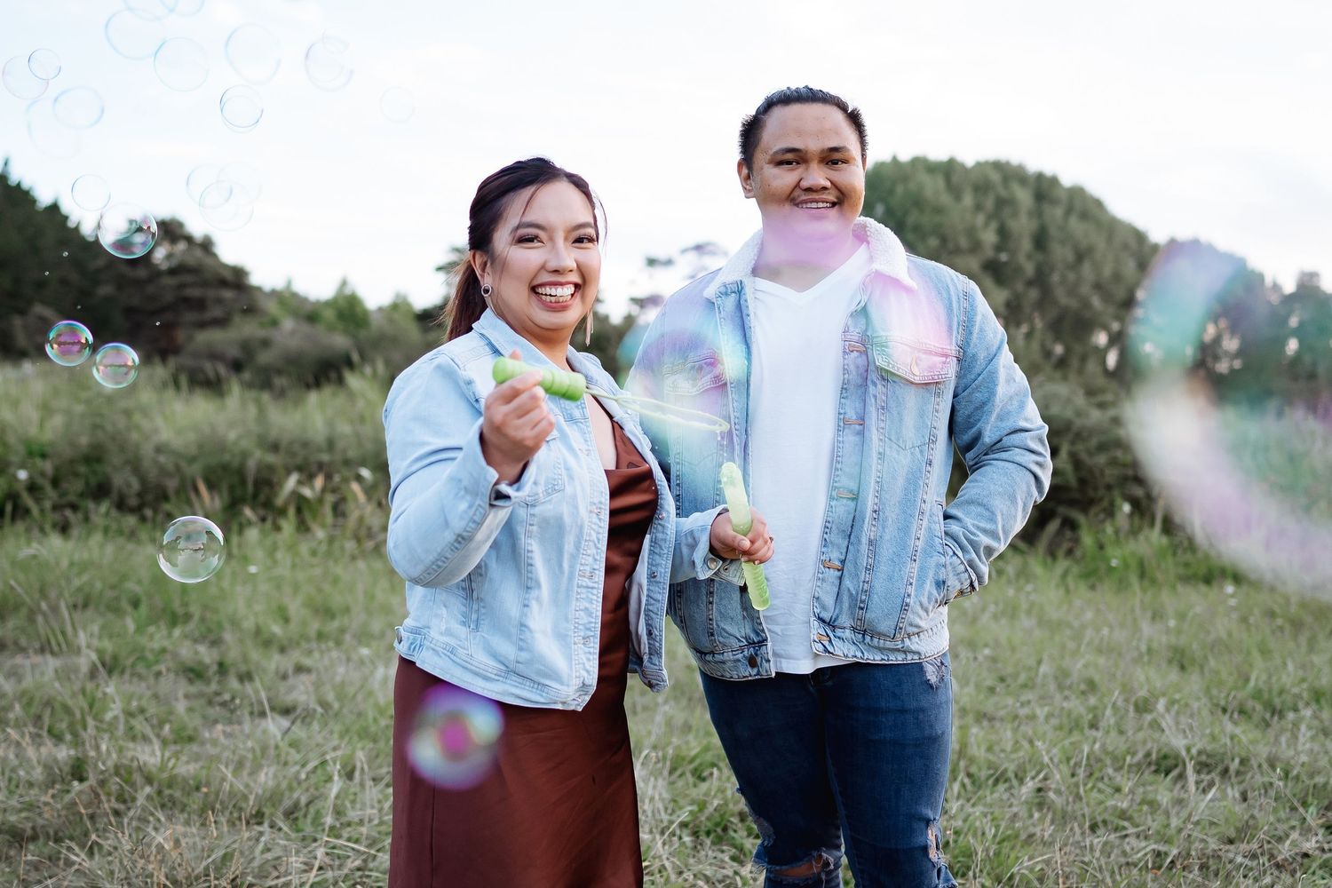 Playful couple blowing bubbles in a grassy field on a sunny day.