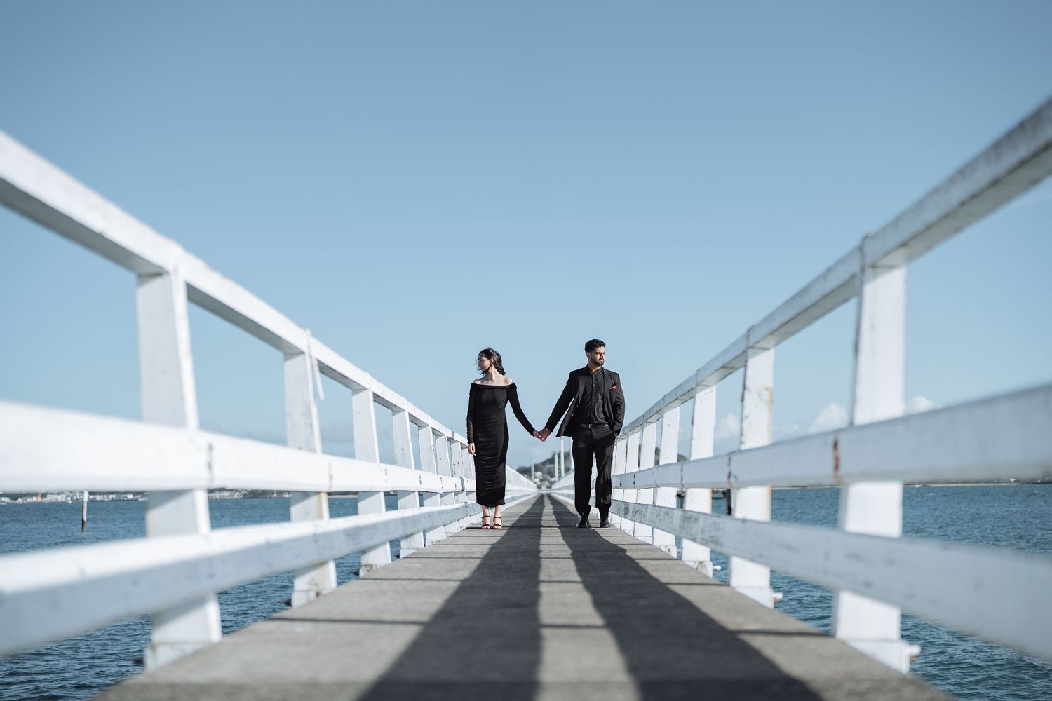 A couple walks along a white pier with water views in the distance.