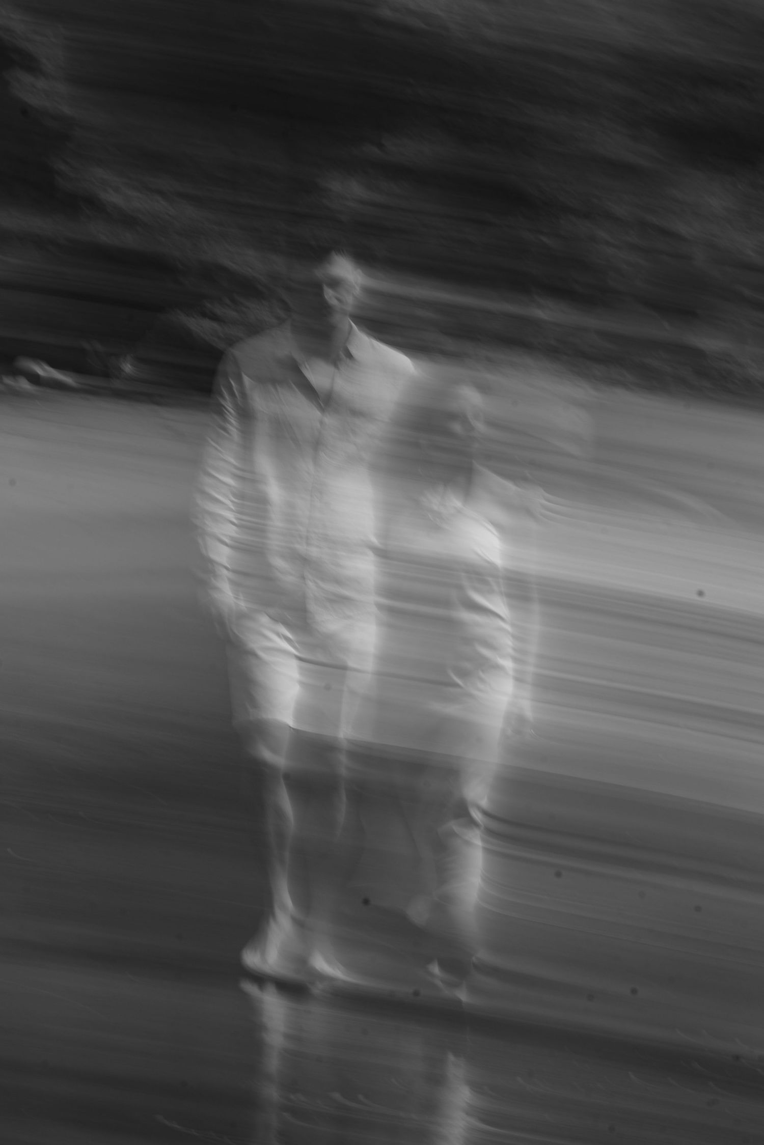 Artistic black and white motion blur photograph of figures walking in an ethereal setting.