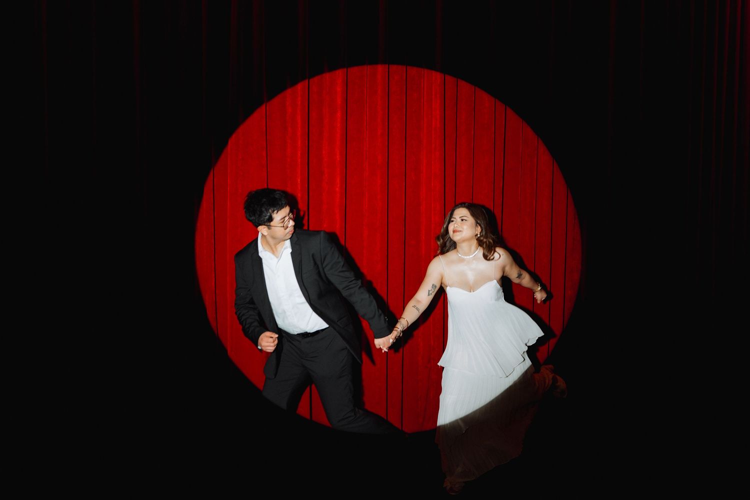 Dramatic spotlight captures dancing couple against red curtain backdrop.