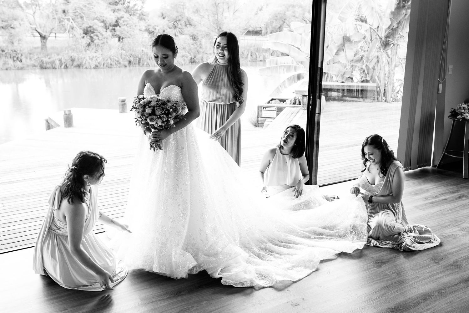Black and white photo of bridal party helping with wedding dress preparations.