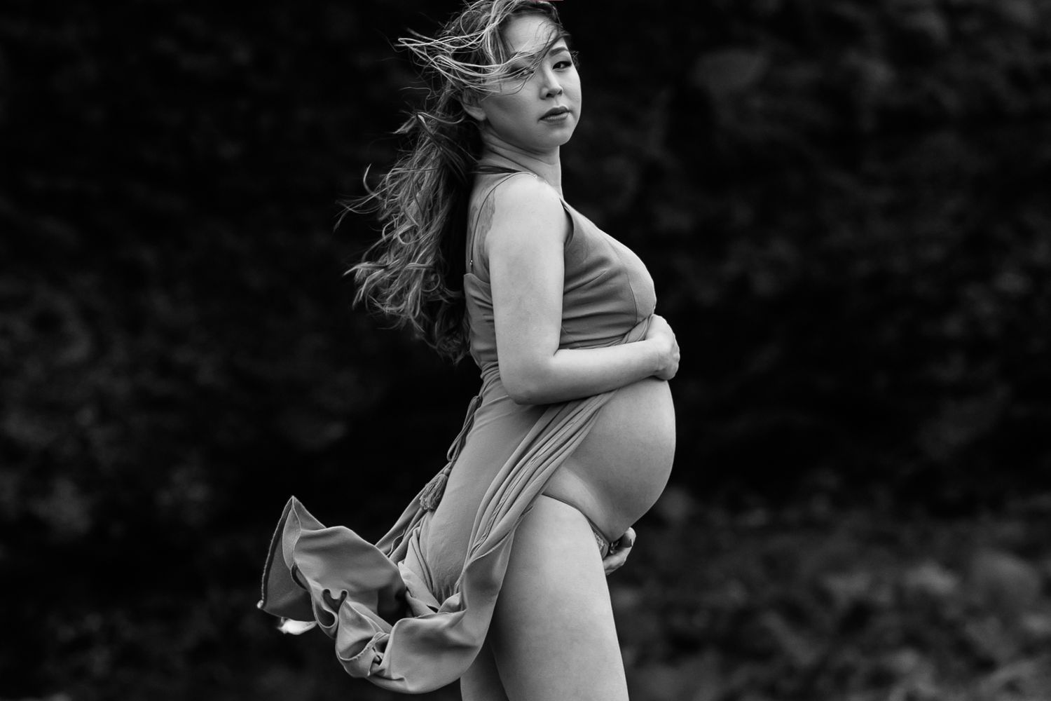 A black and white maternity portrait with flowing fabric caught in dramatic motion.