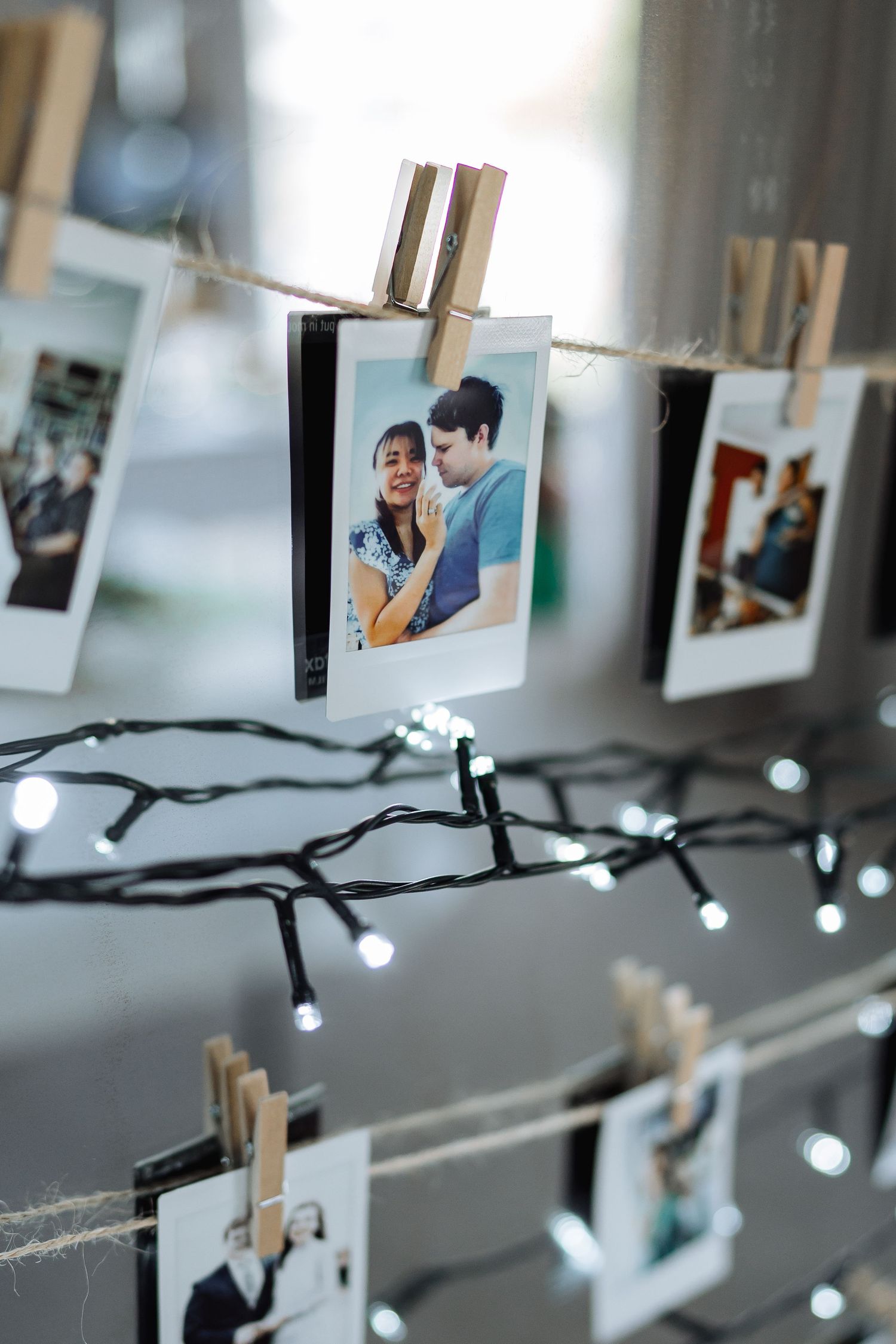 String lights illuminate a collection of photos hanging from twine with wooden clothespins in a dreamy display.
