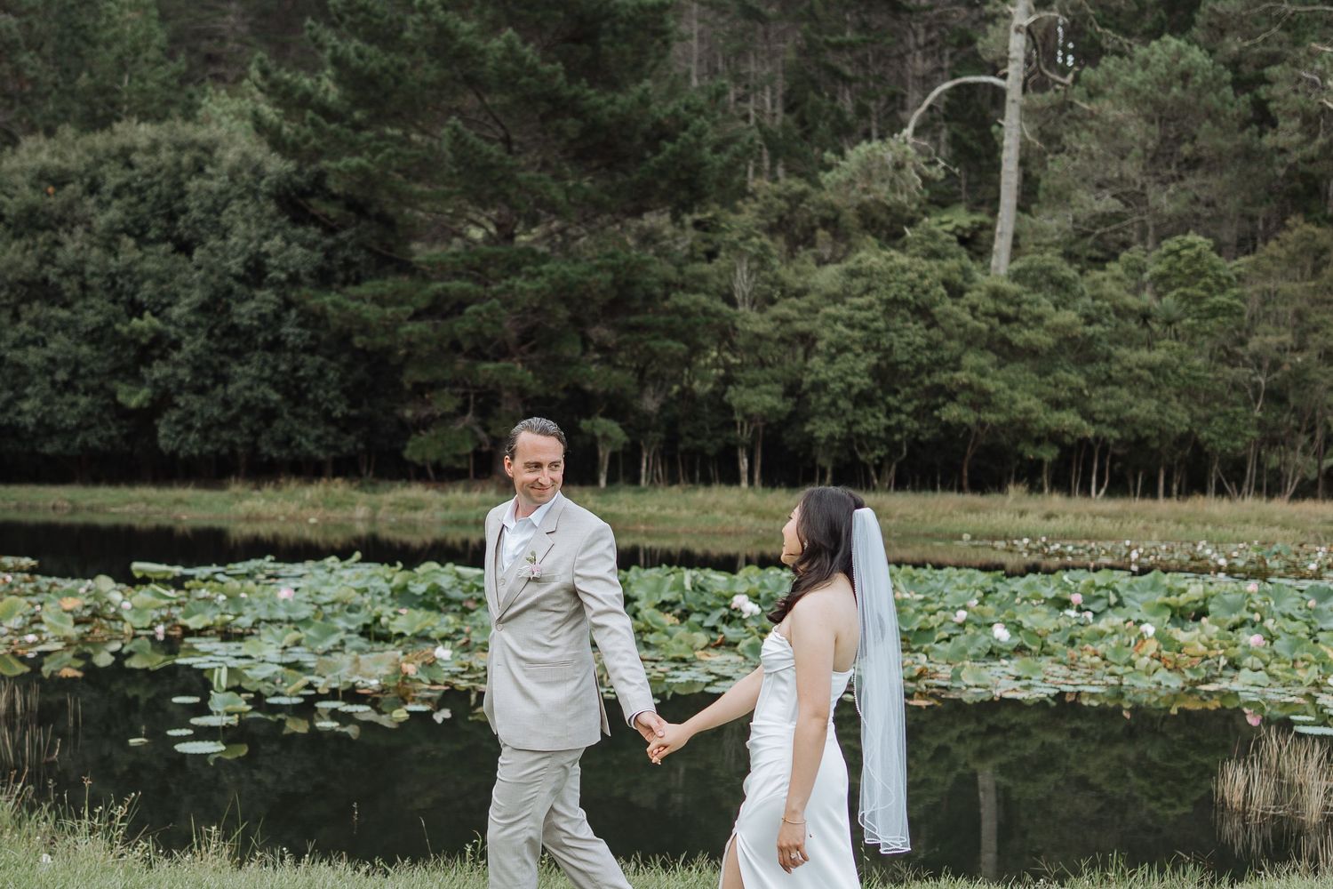Couple shares intimate moment on white platform with pond and forest landscape in background.