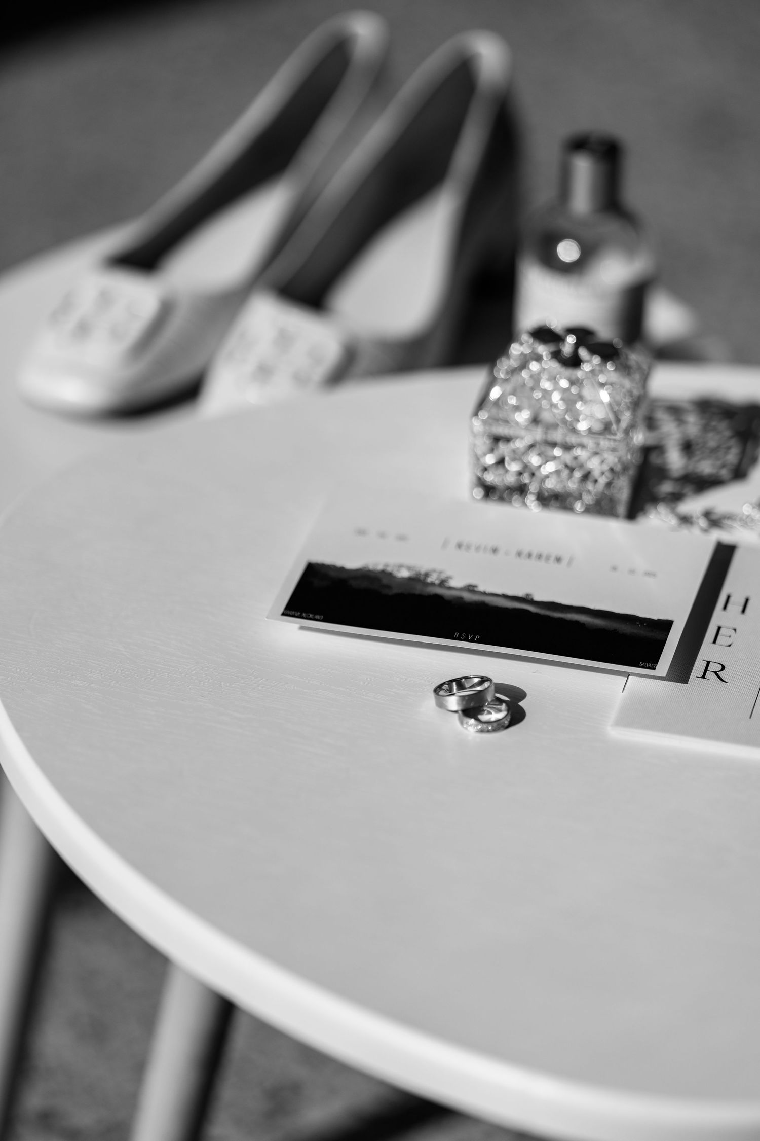 Close-up black and white photo of wedding rings and details on a white surface.