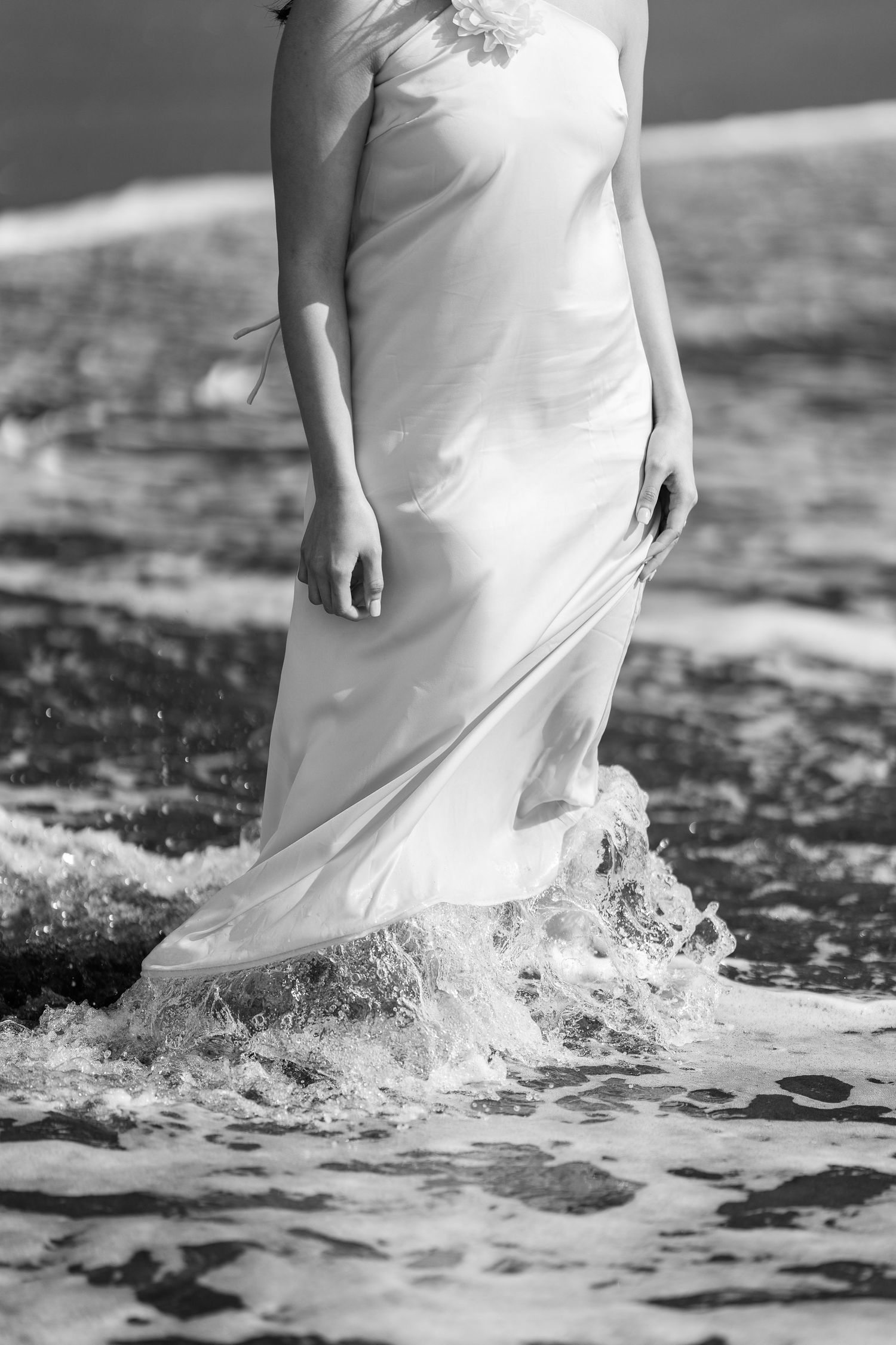 White dress flowing in ocean waves creating dramatic water splashes on beach.