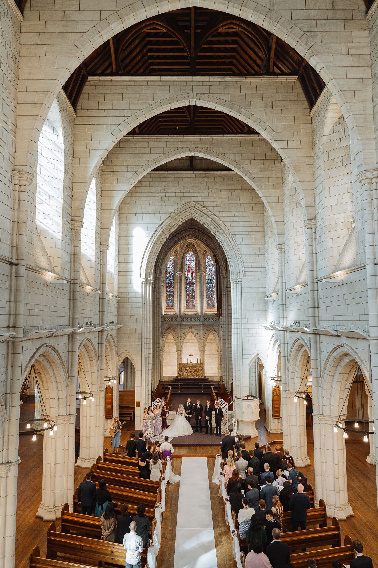 Interior of Gothic church with vaulted ceilings and wooden pews during a wedding ceremony.