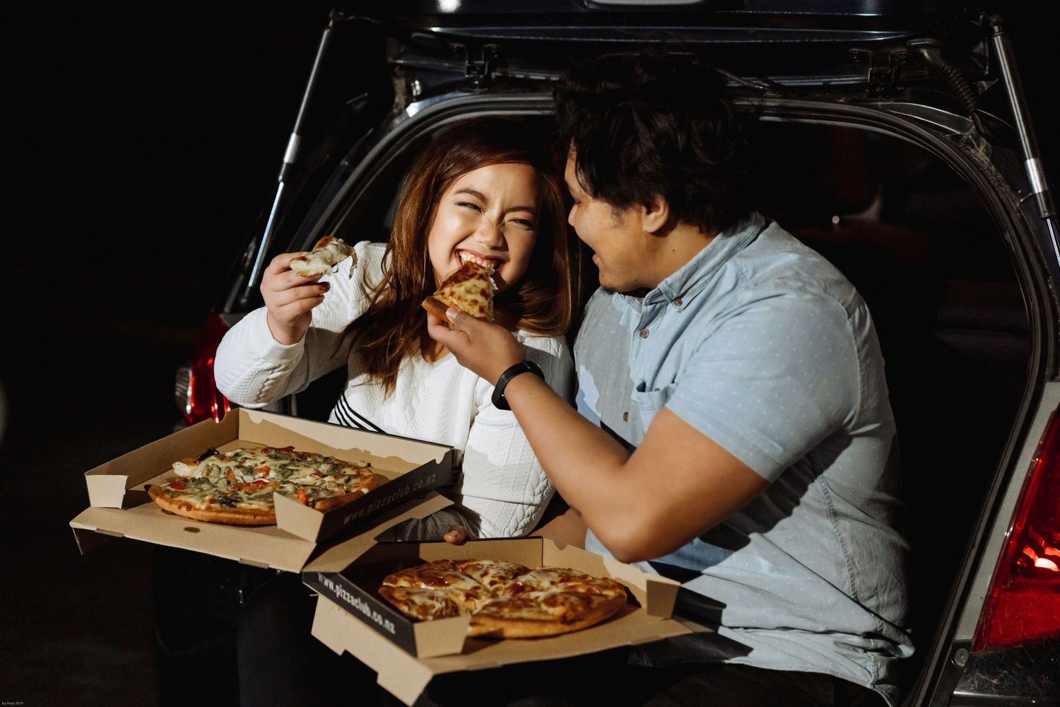 Couple sharing pizza and laughing together in a car.