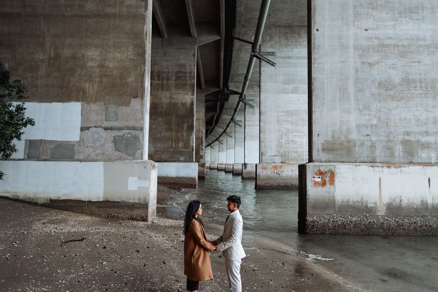 A couple stands against an industrial concrete wall background.
