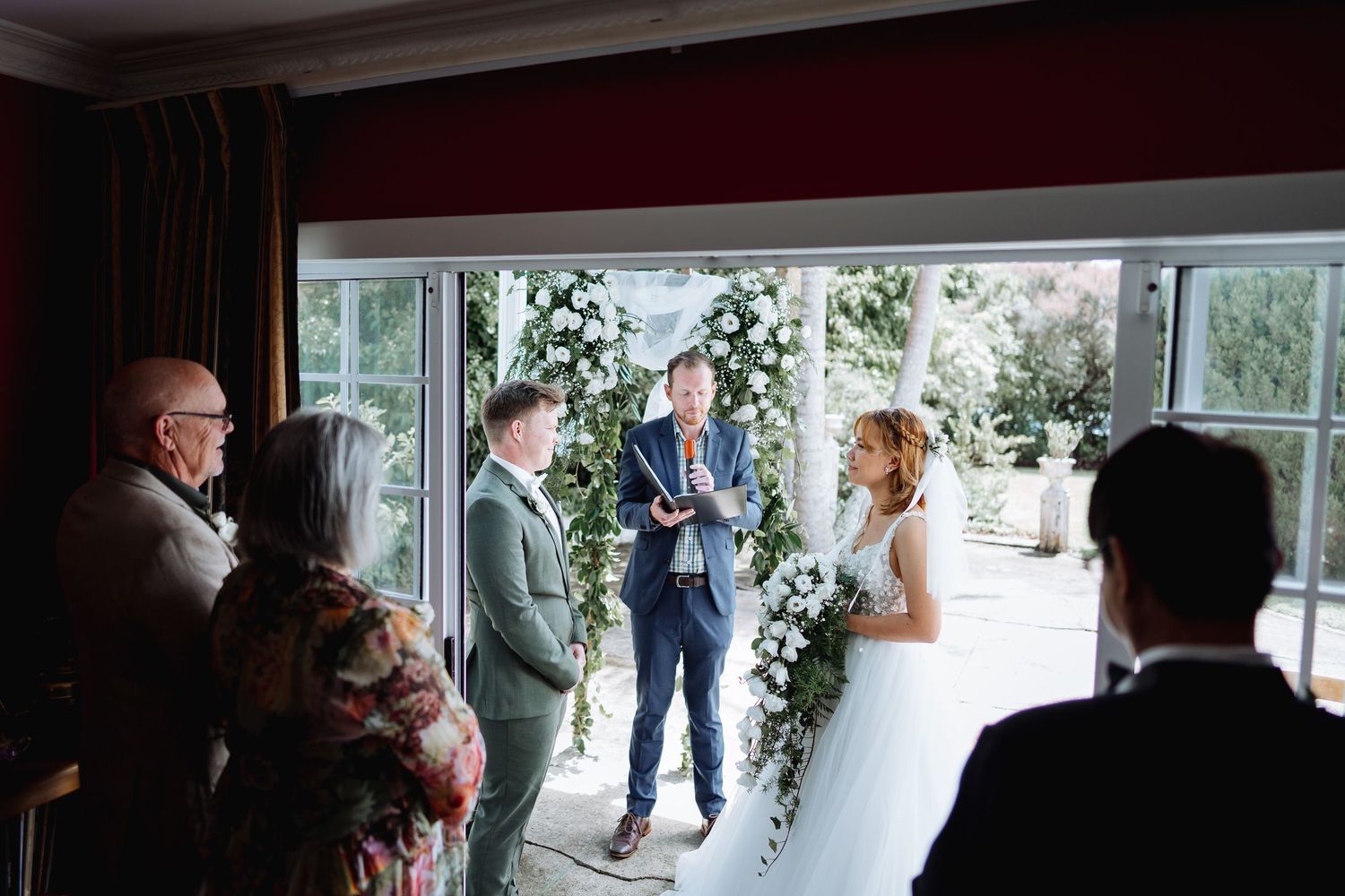 Wedding ceremony guests gathered in a bright sunlit room with large windows.
