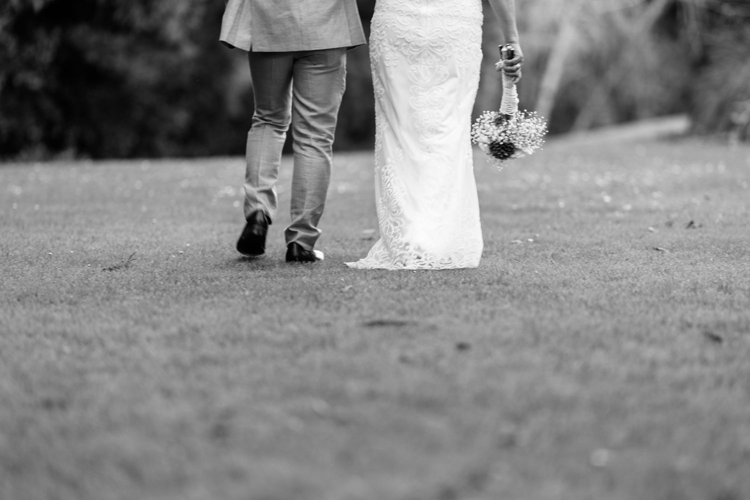 Black and white photo of bride and groom's feet walking together on grass.