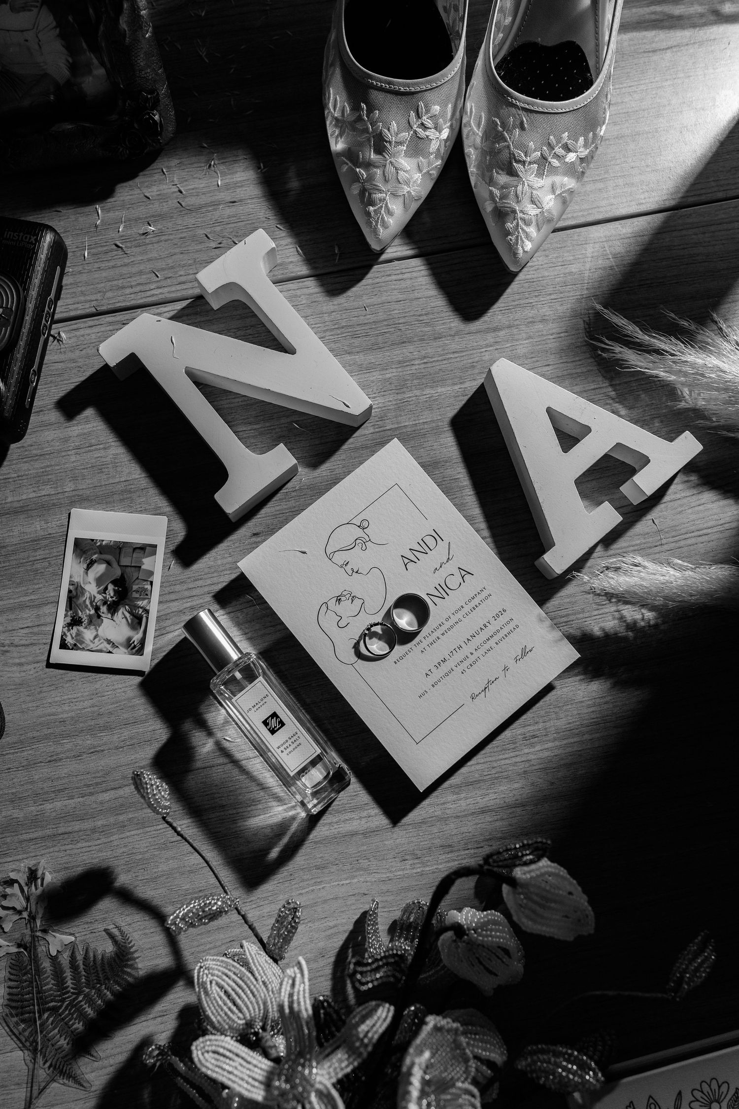 Black and white photo of wedding decorations and personal items arranged on wood table.