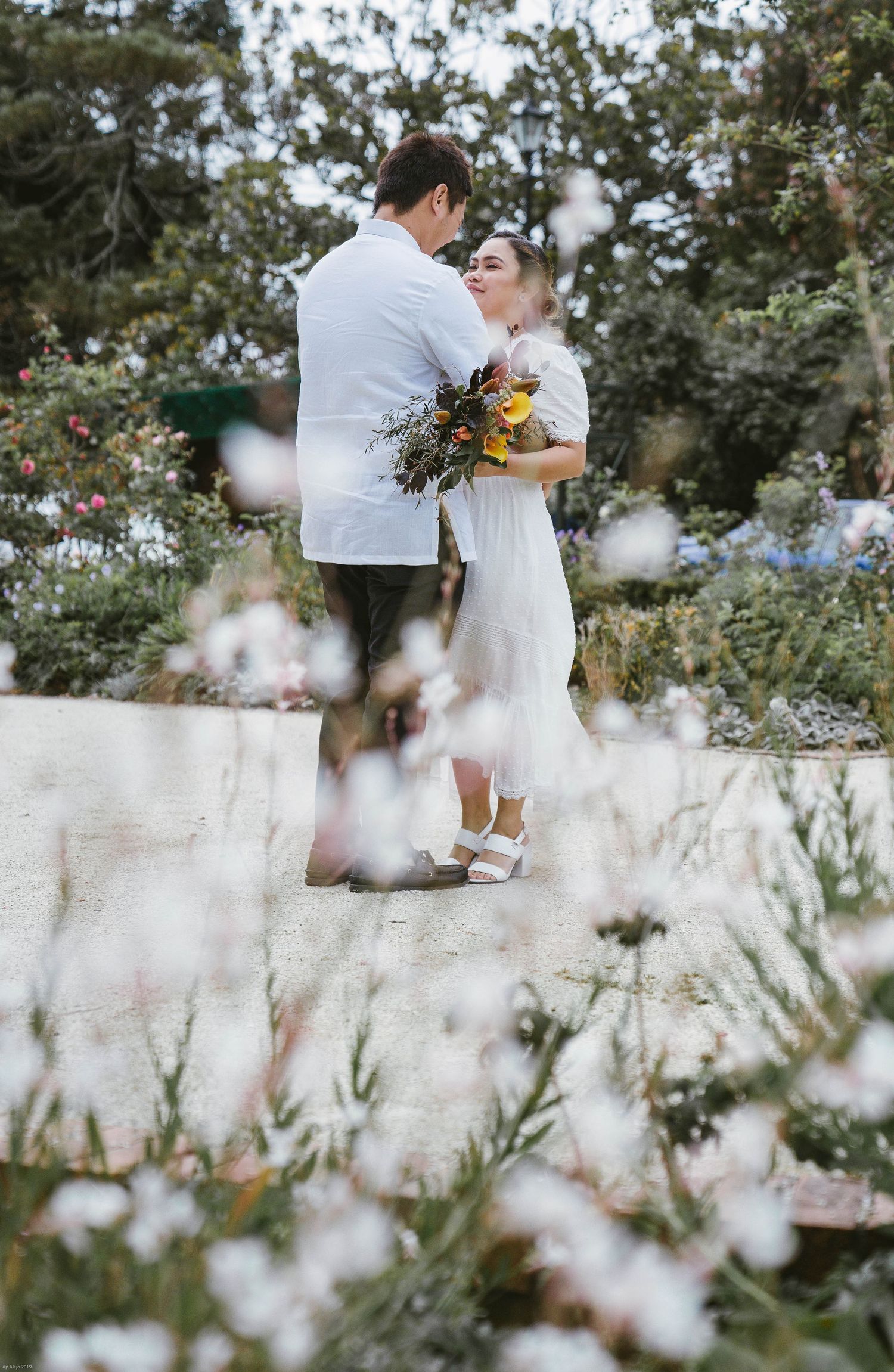 A couple embraces in a garden setting surrounded by delicate white flowers and greenery.