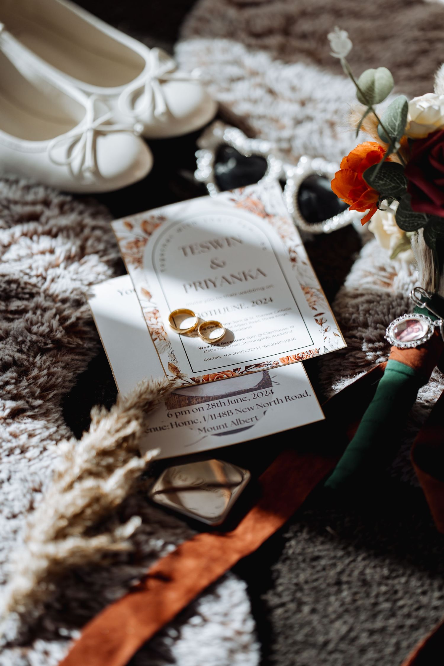 Wedding invitation and rings arranged artistically on textured fabric with floral accents.
