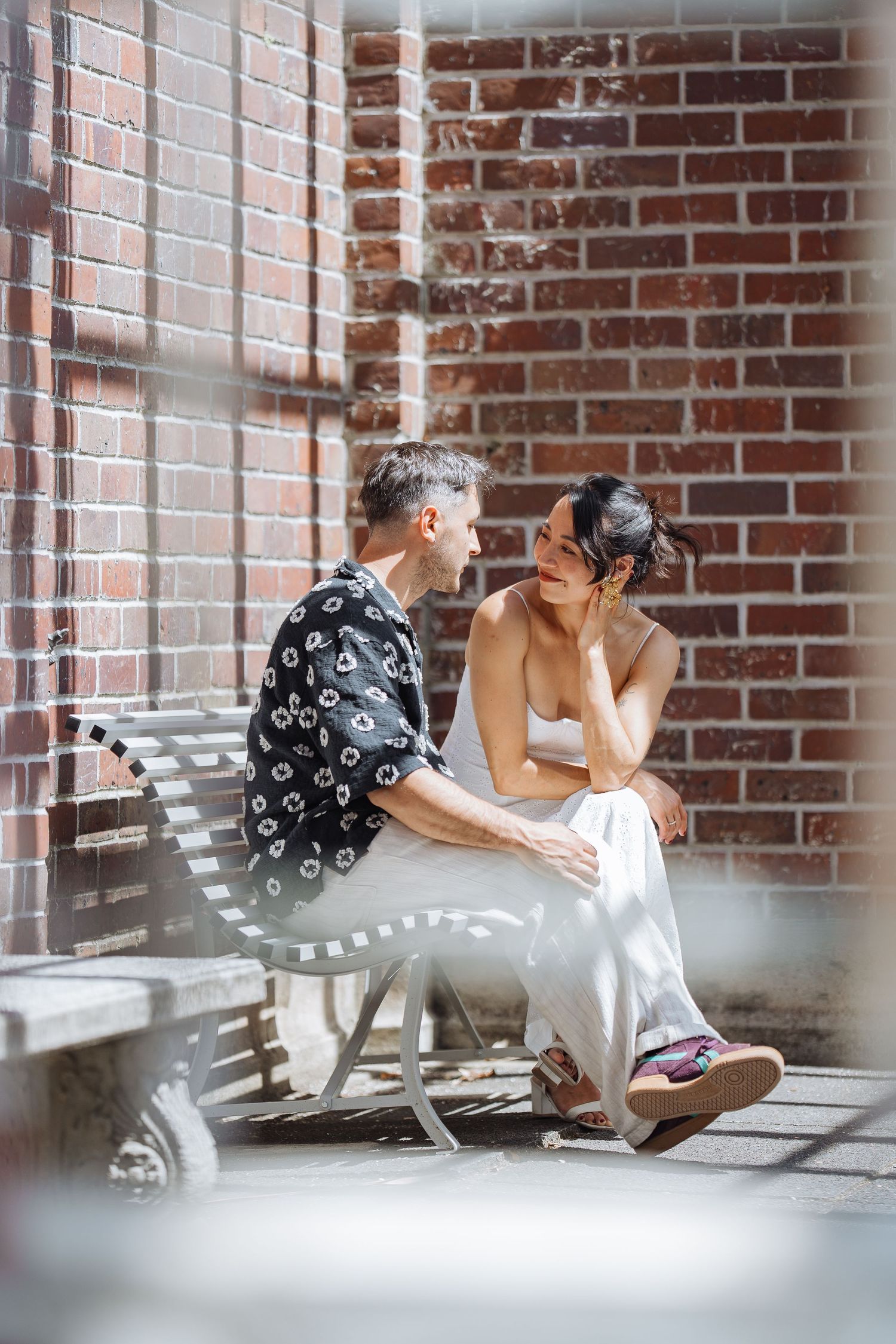 A couple shares intimate moments on a white bench against a rustic brick wall.
