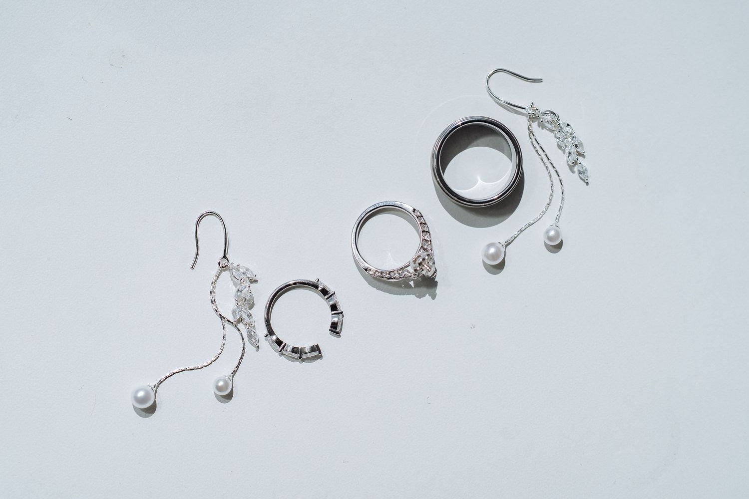 Wedding jewelry and accessories including earrings and bracelets arranged on light gray background.