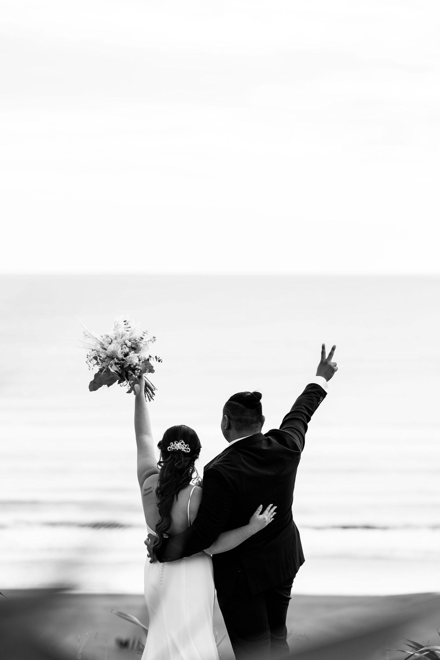 Silhouetted couple celebrates with raised arms against ocean horizon.