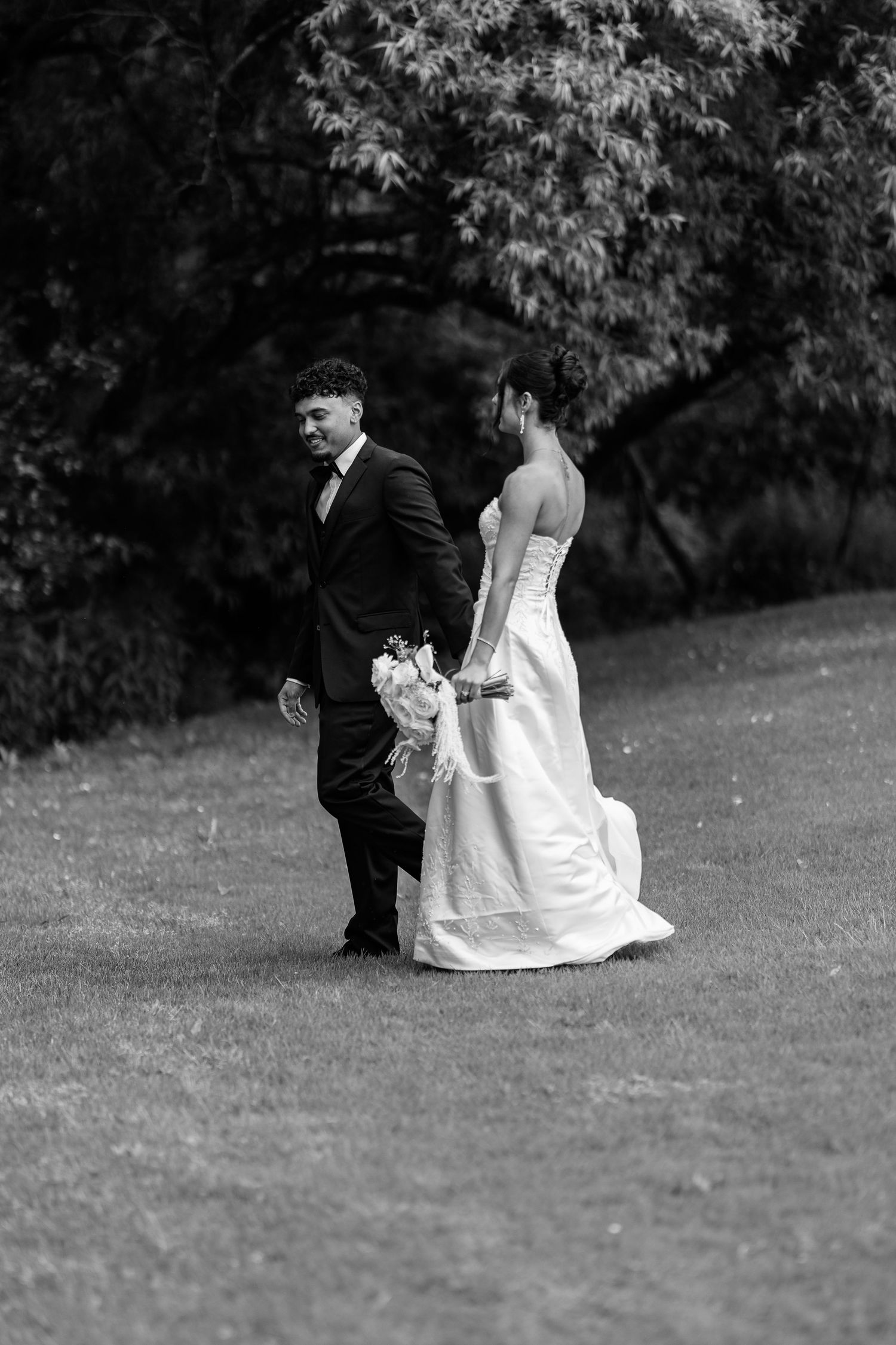 Couple in wedding attire walking together on grassy lawn.