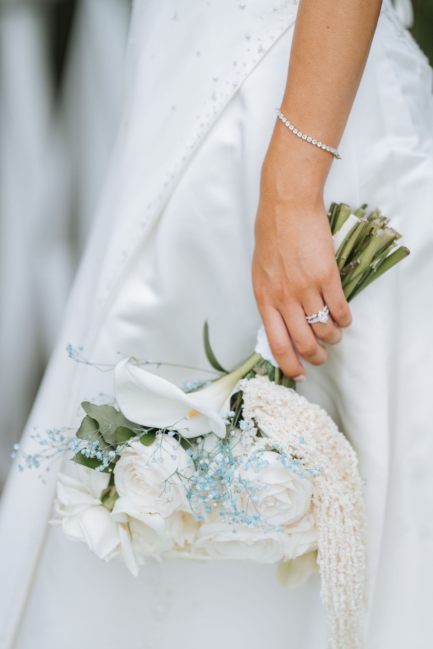 Close-up of bridal hands holding delicate white and blue floral bouquet with pearl details.
