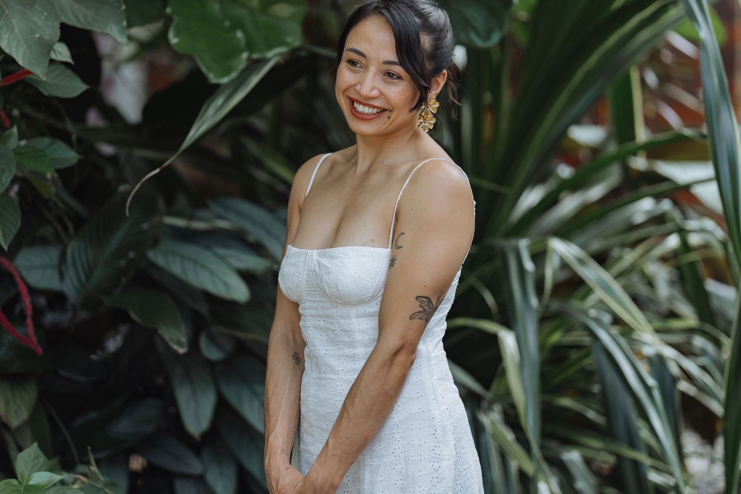 A person in a white summer dress stands among lush tropical foliage and greenery.