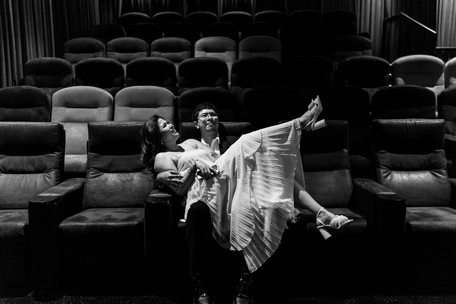 Artistic black and white photo of couple posing dramatically in theater seats.