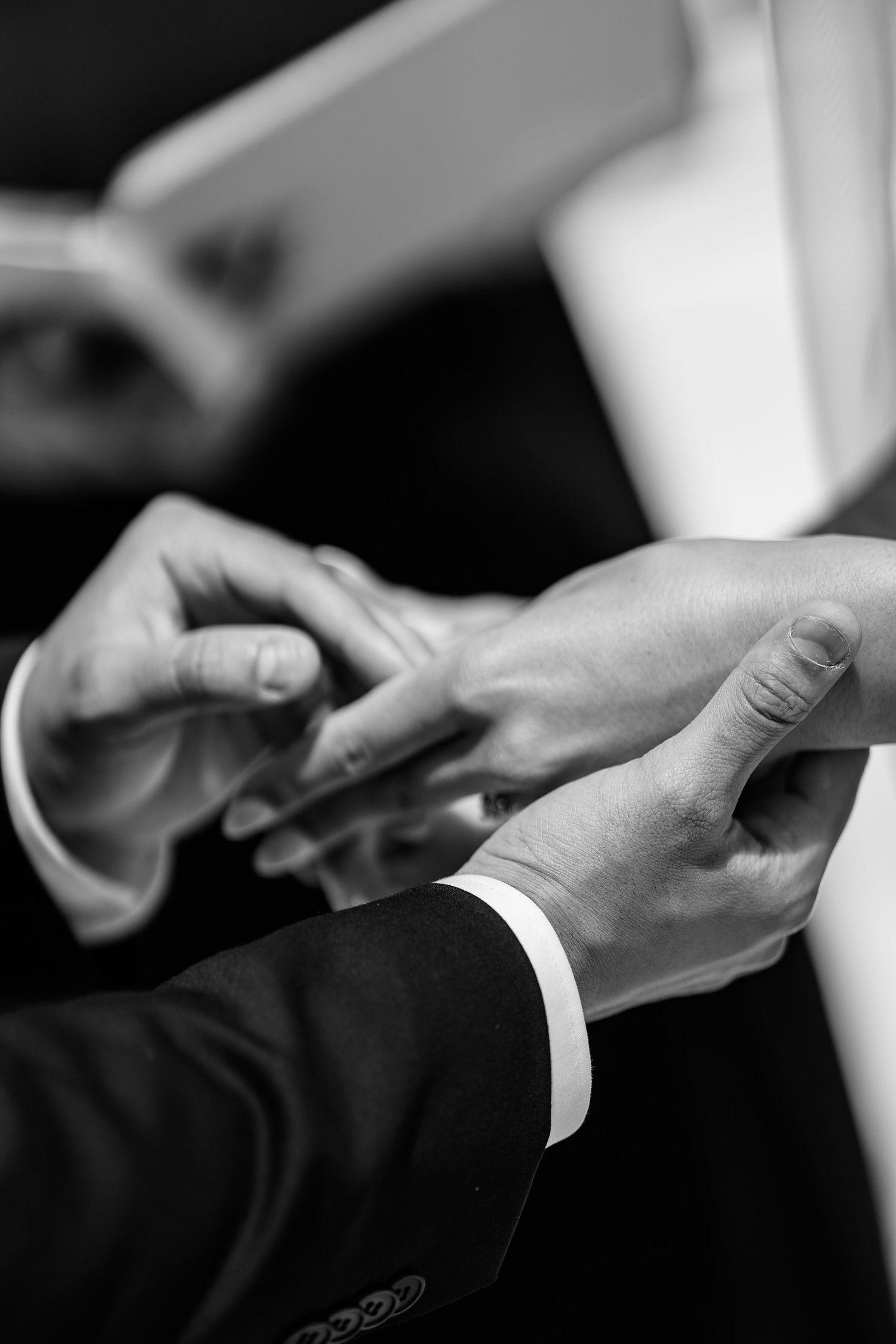 Black and white detail shot of hands joining together in formal attire.