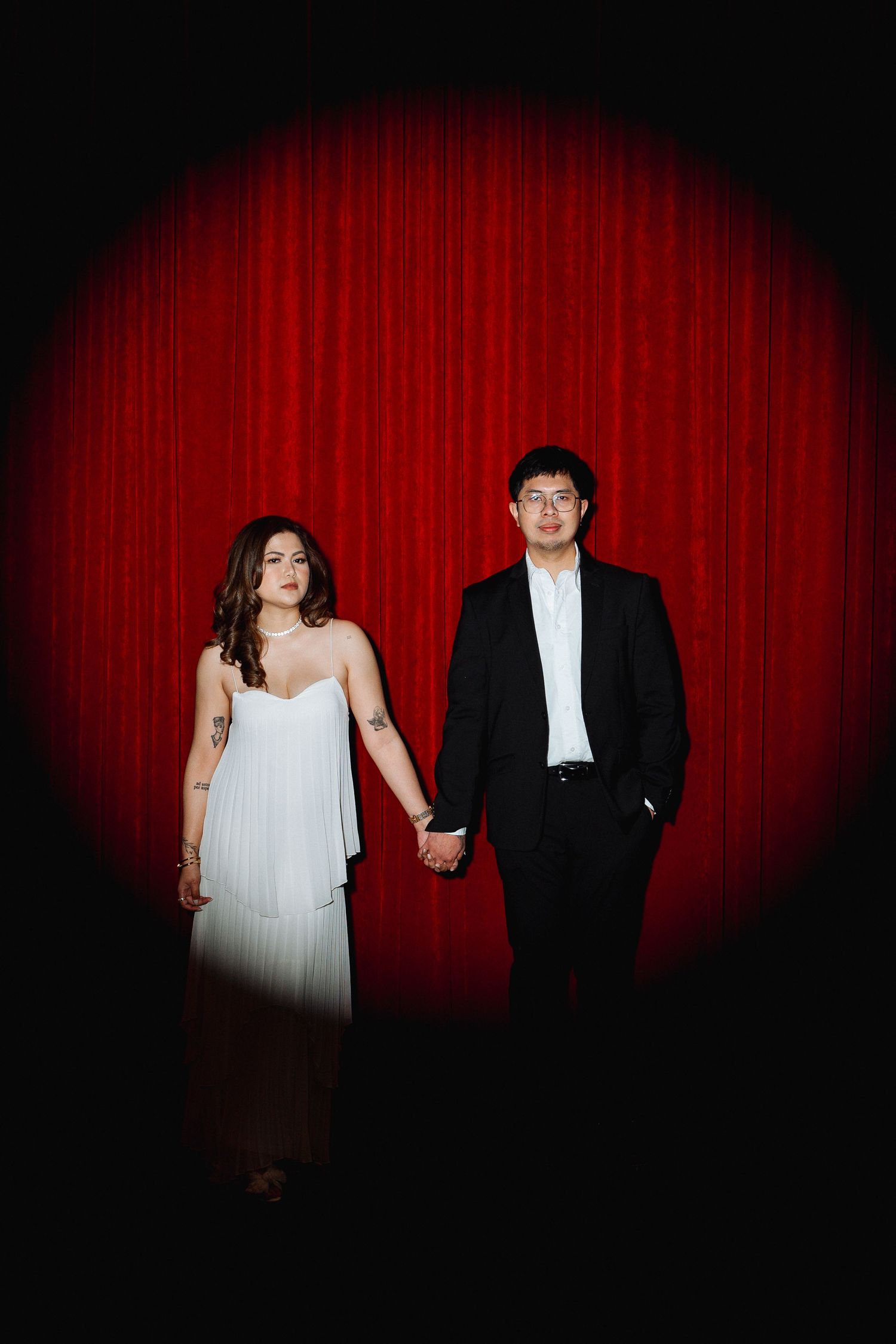 Dramatic portrait against red curtain backdrop with couple in formal attire.