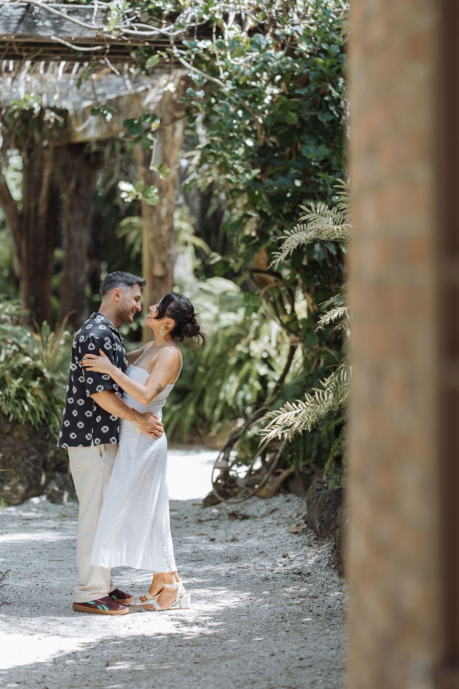 A couple sits together on a garden path surrounded by lush greenery and trees.