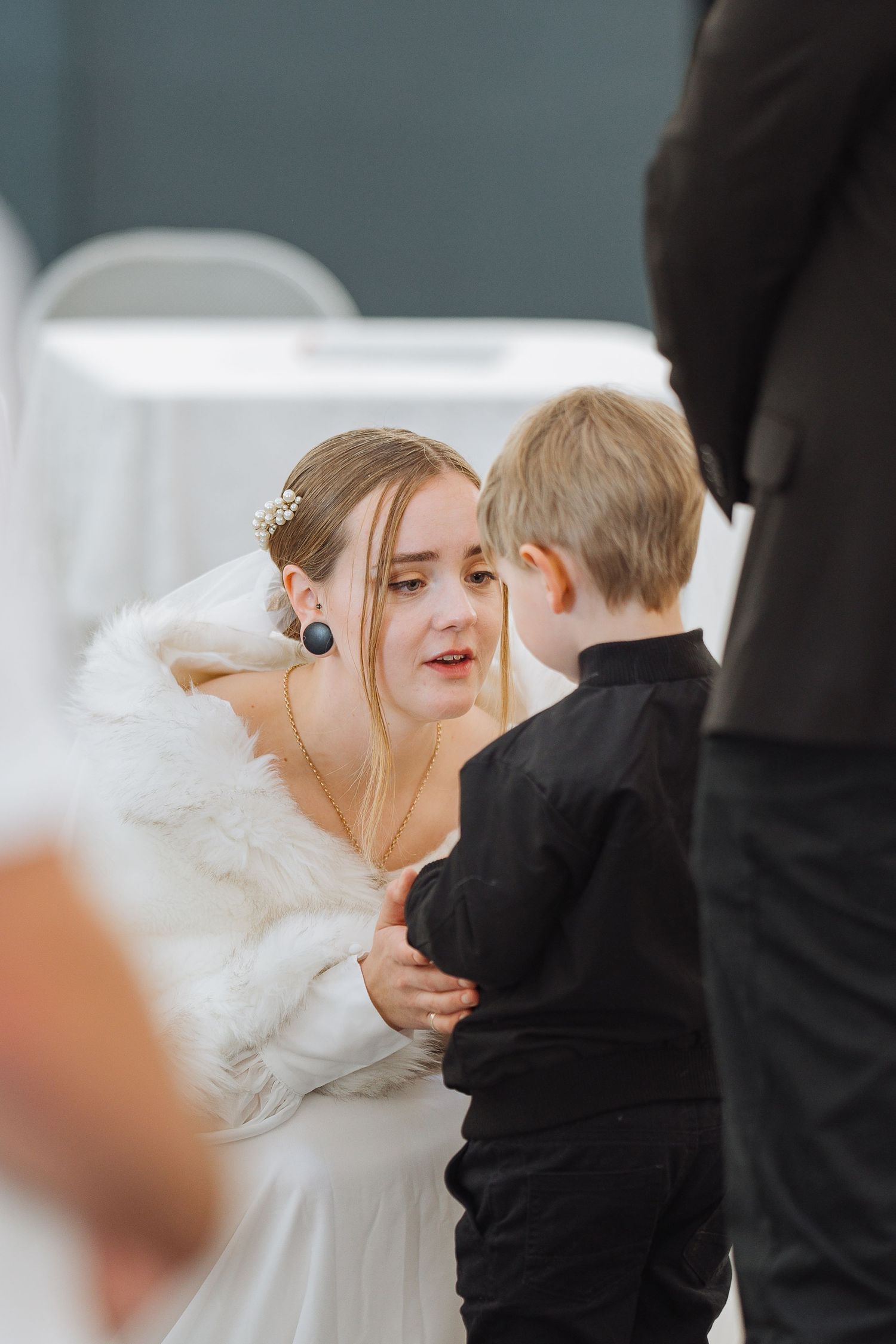 A tender moment between a bride in white and a young boy in formal wear during a wedding ceremony.