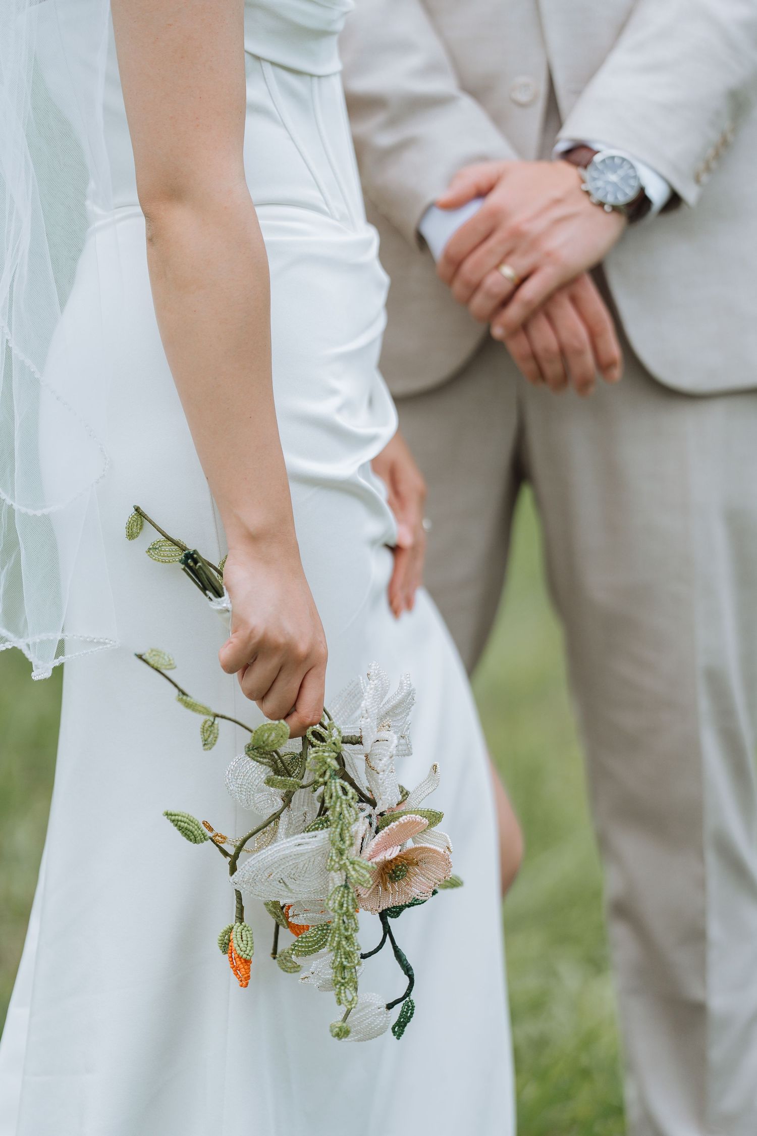 Close-up of bride in white dress holding delicate flowers while standing next to groom in light suit.