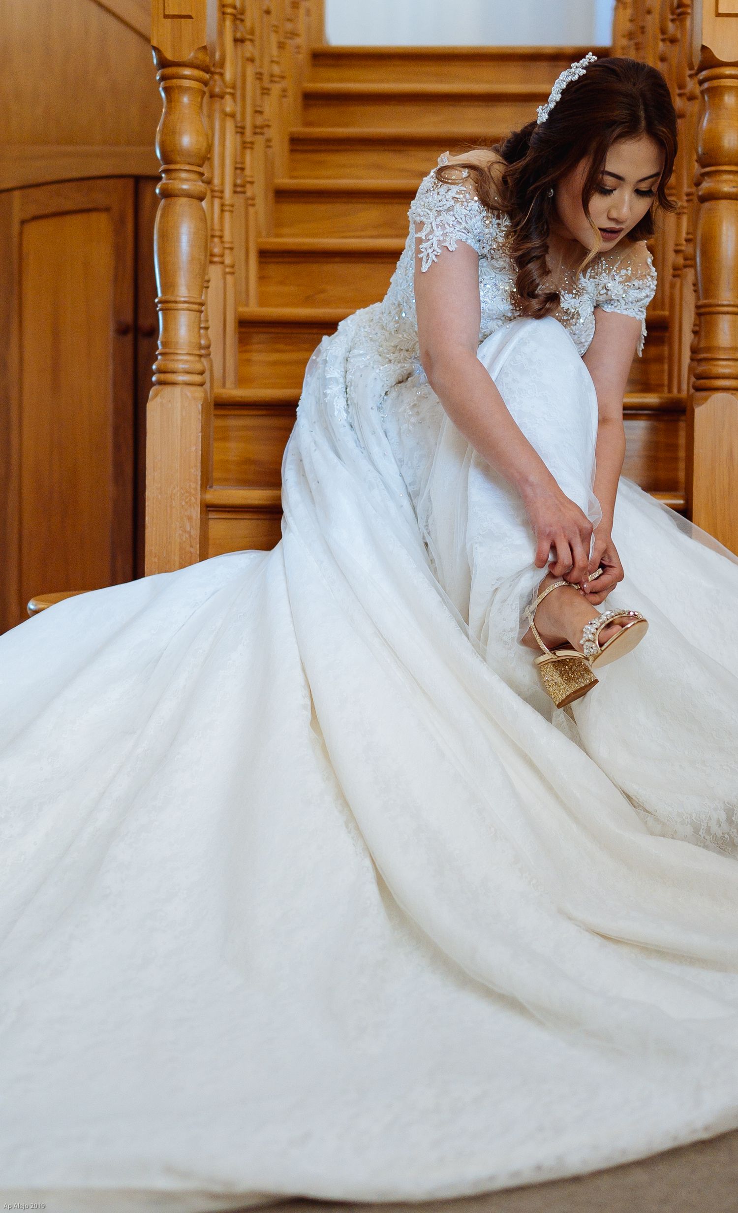 Close-up of ornate white wedding dress with lace details cascading down wooden stairs.