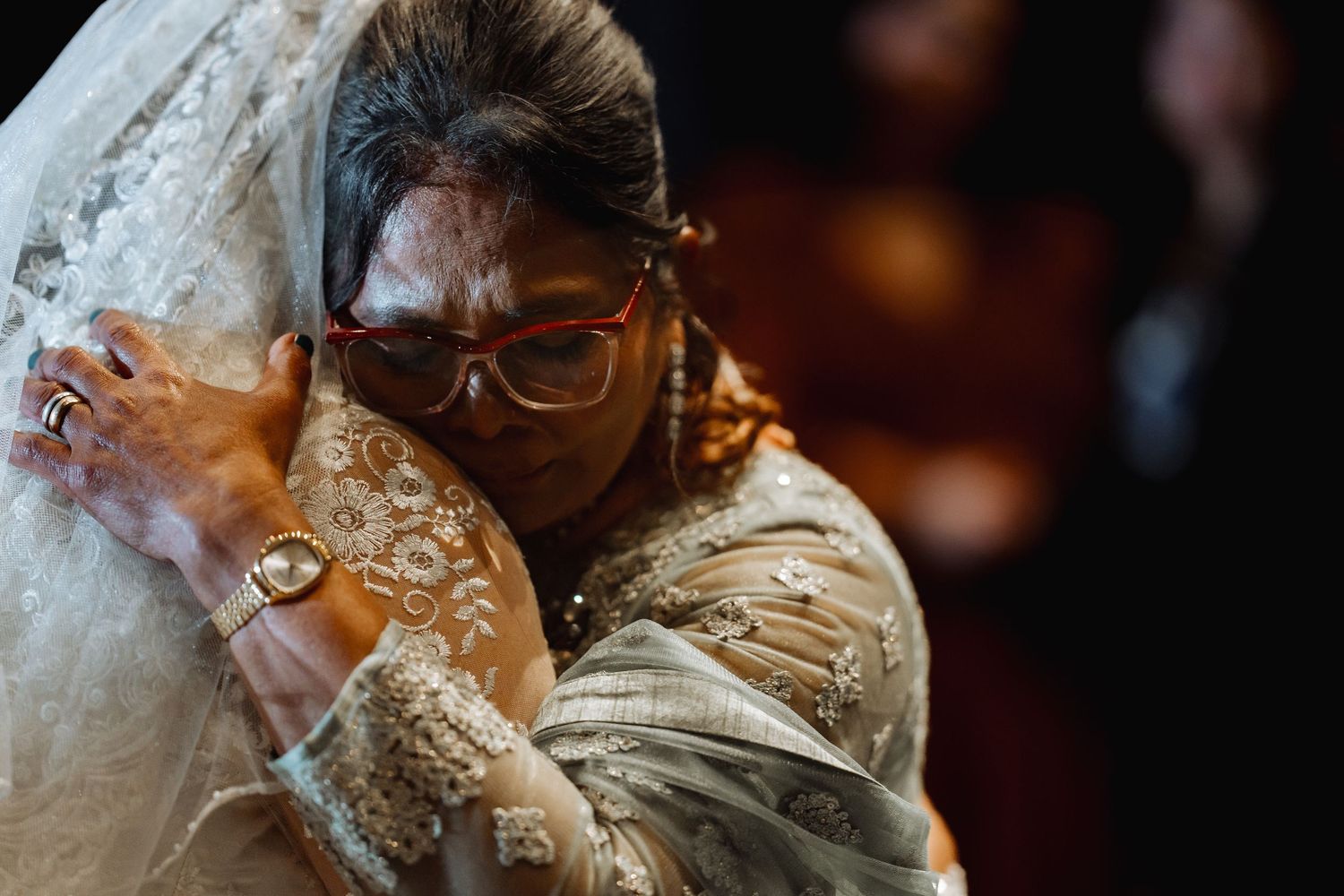 Emotional embrace between wedding guest and bride in detailed lace dress.