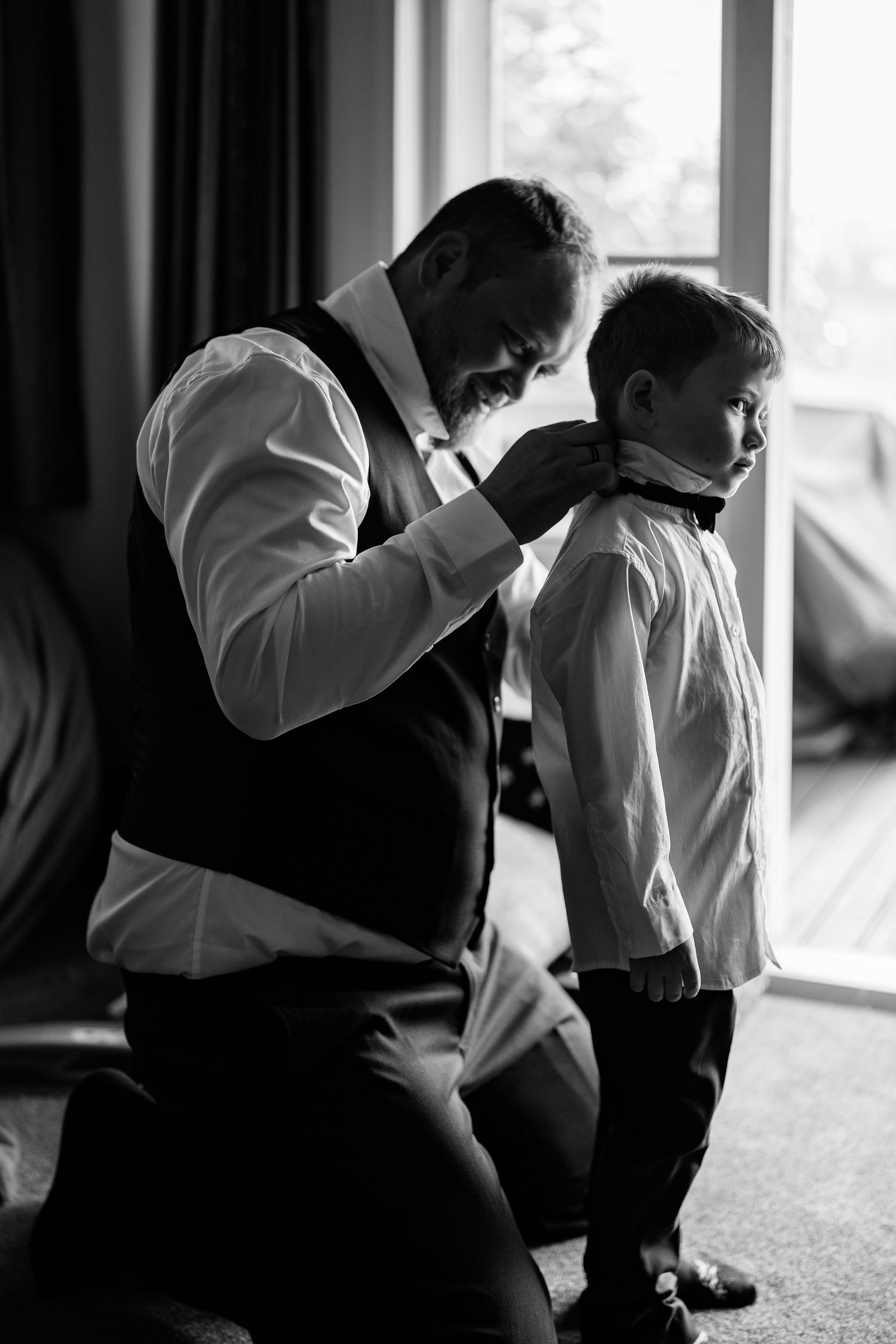 A touching black and white moment of wedding preparation between two people adjusting formal attire.