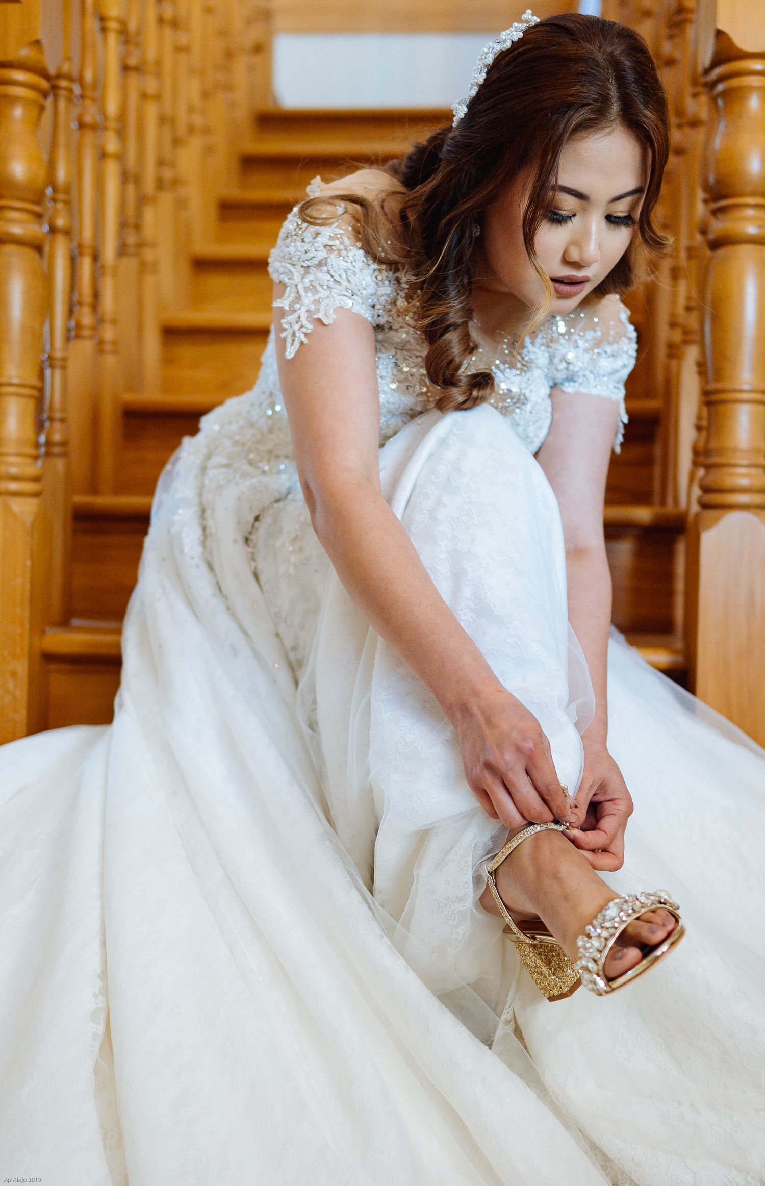 Close-up details of a white lace wedding dress with ornate beading near wooden stairs.