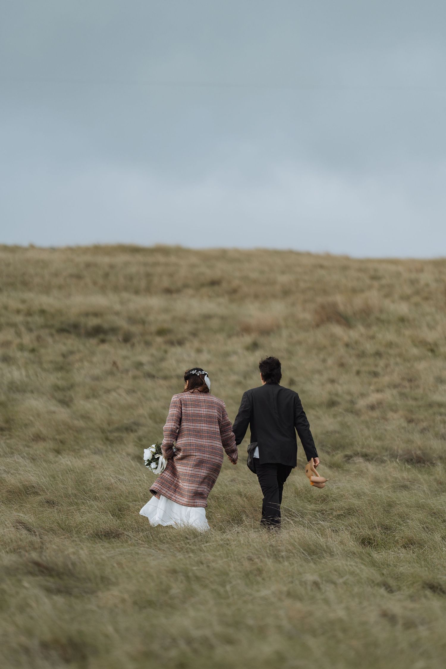 A couple sits together on a grassy hillside overlooking the ocean.