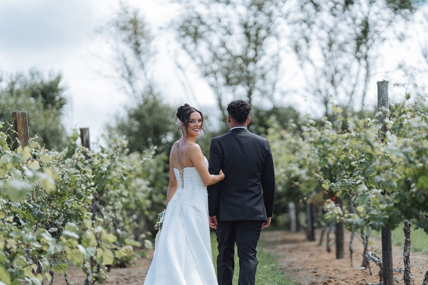 Newlyweds walking through an orchard with rows of blooming trees.