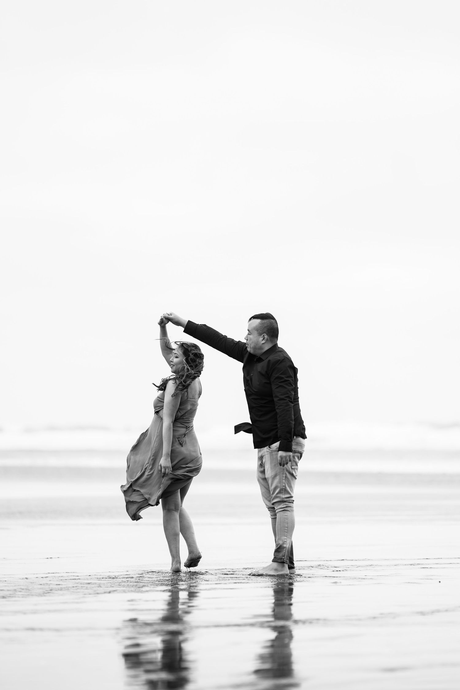 A black and white photo of a couple dancing on a misty beach.