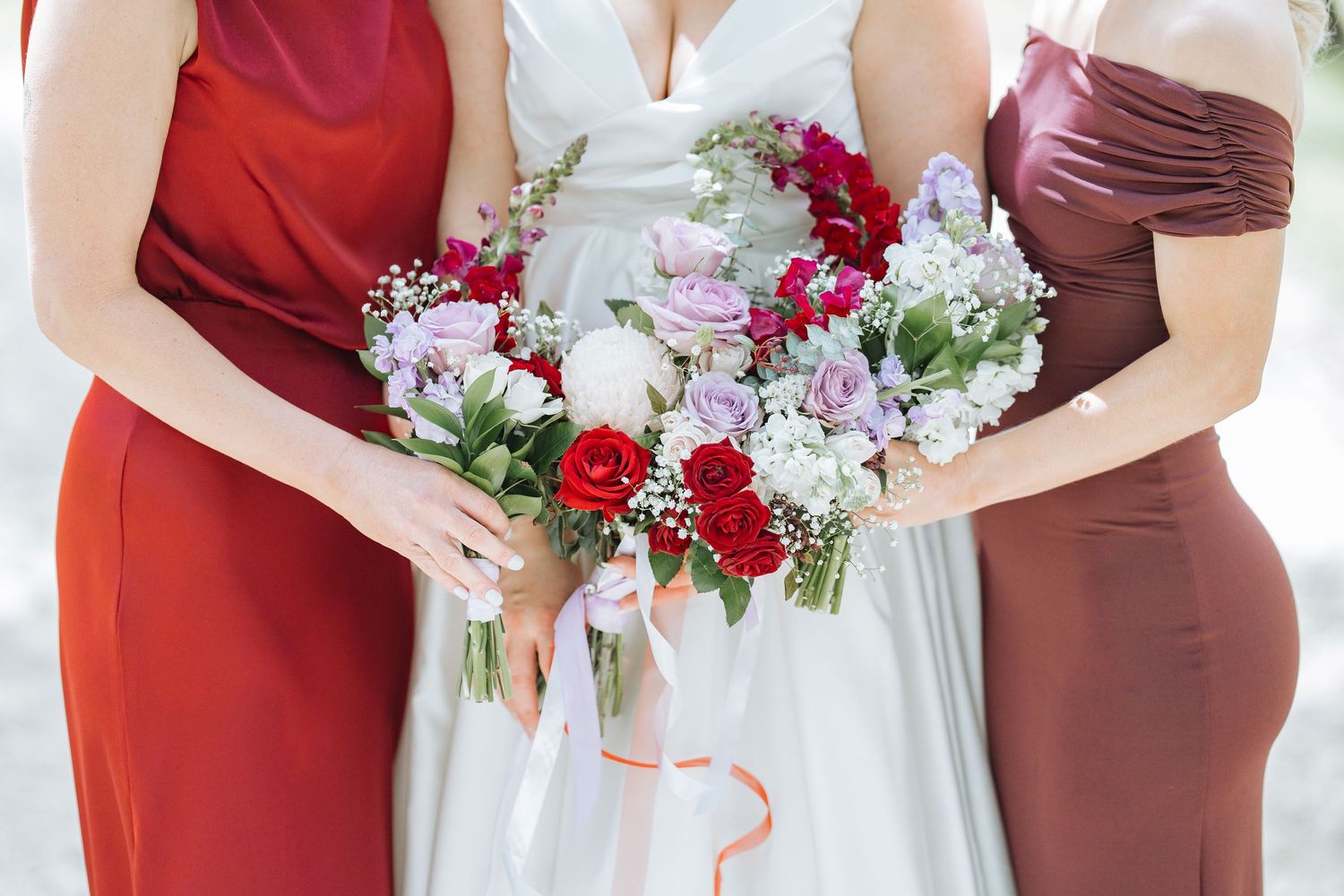 Close-up of wedding bouquets with red and white flowers held by people in burgundy and white dresses.