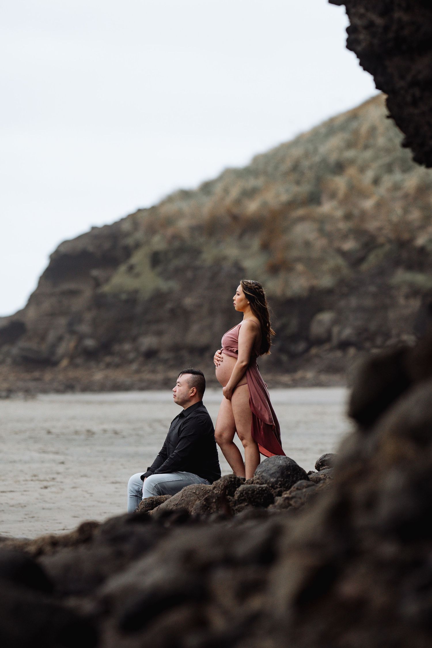 Couple resting on rocky beach overlooking coastal cliffs at sunset.