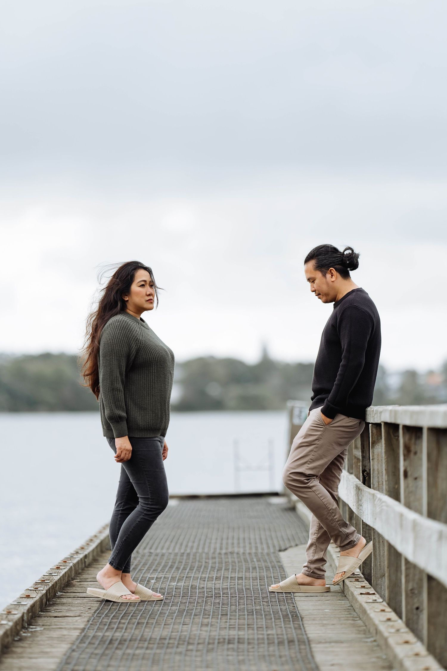 Couple performing playful movements on a wooden pier by the water.