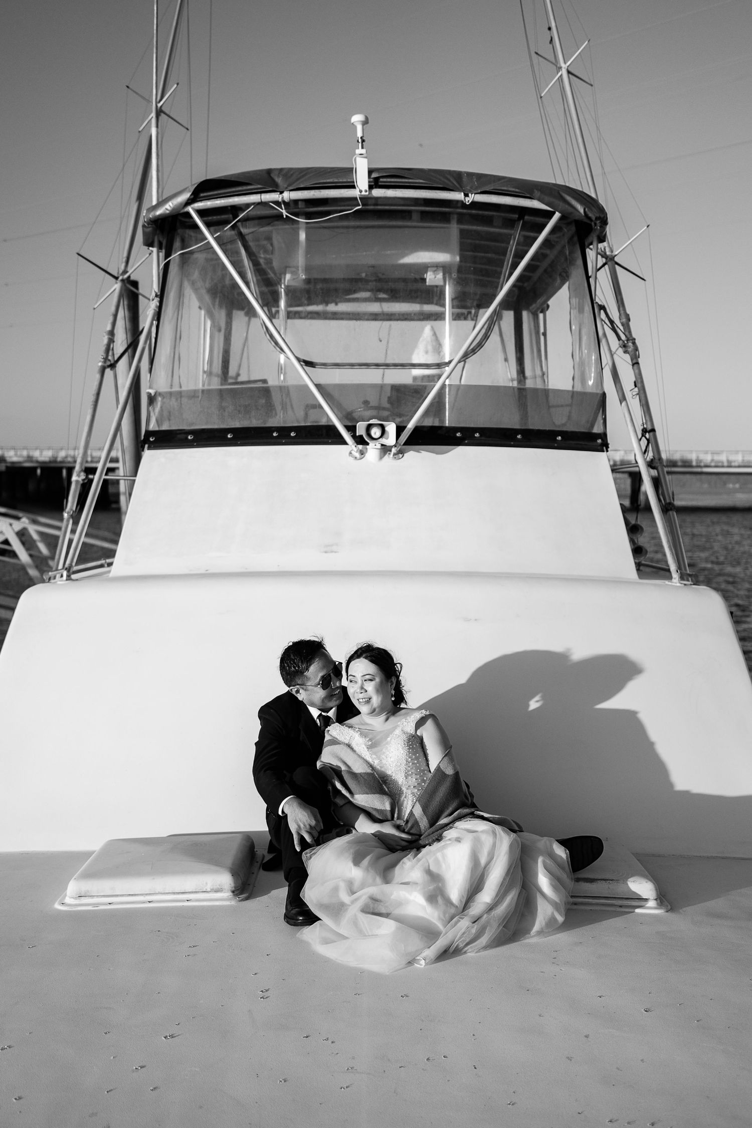A couple in wedding attire shares an intimate moment on the deck of a yacht.