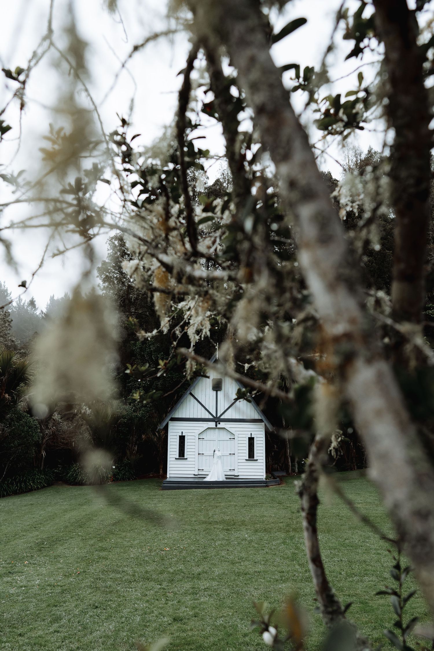 Small white chapel nestled among trees in a serene garden setting.