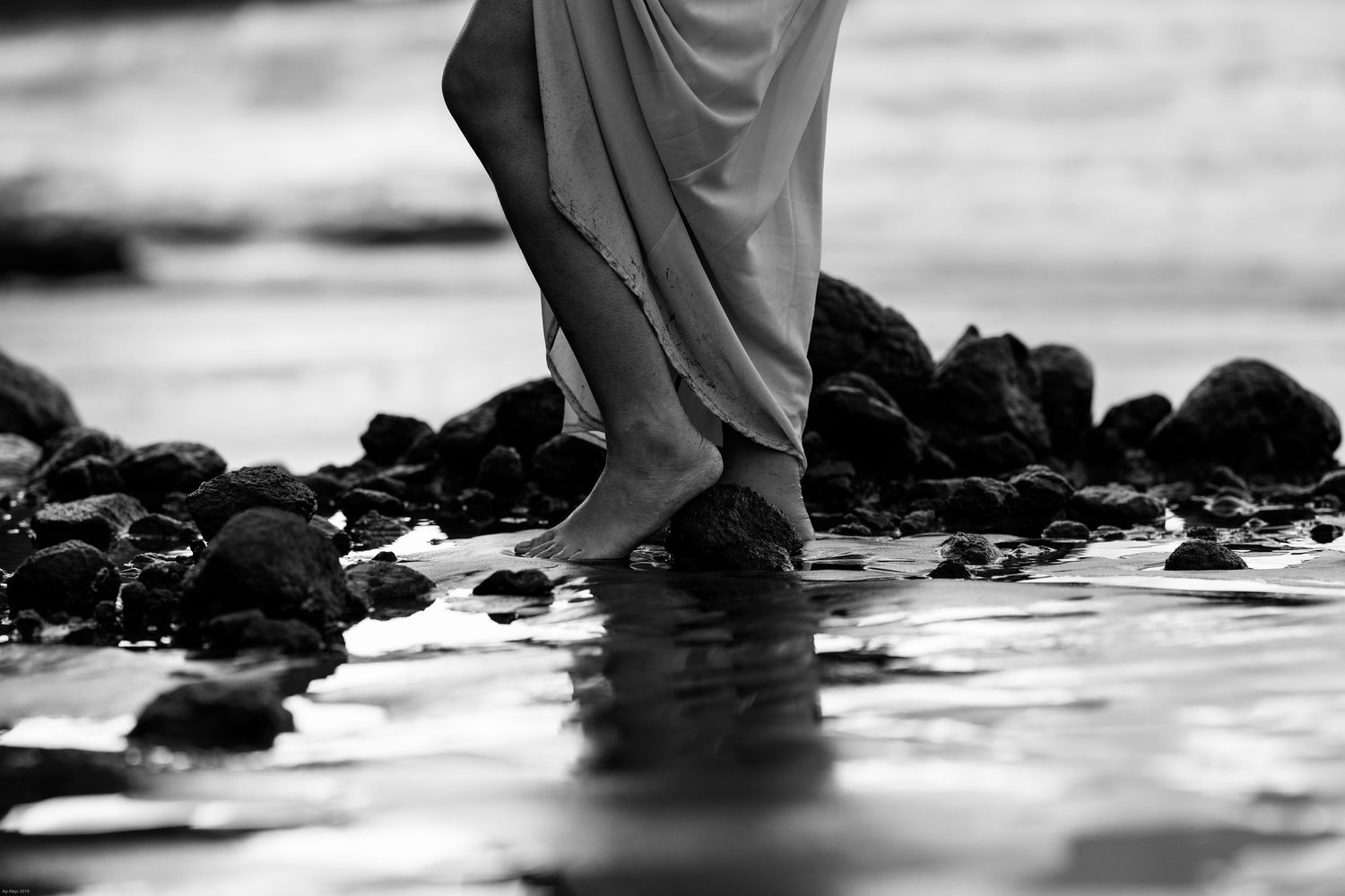 Black and white artistic photo of feet standing in shallow water among rocks.