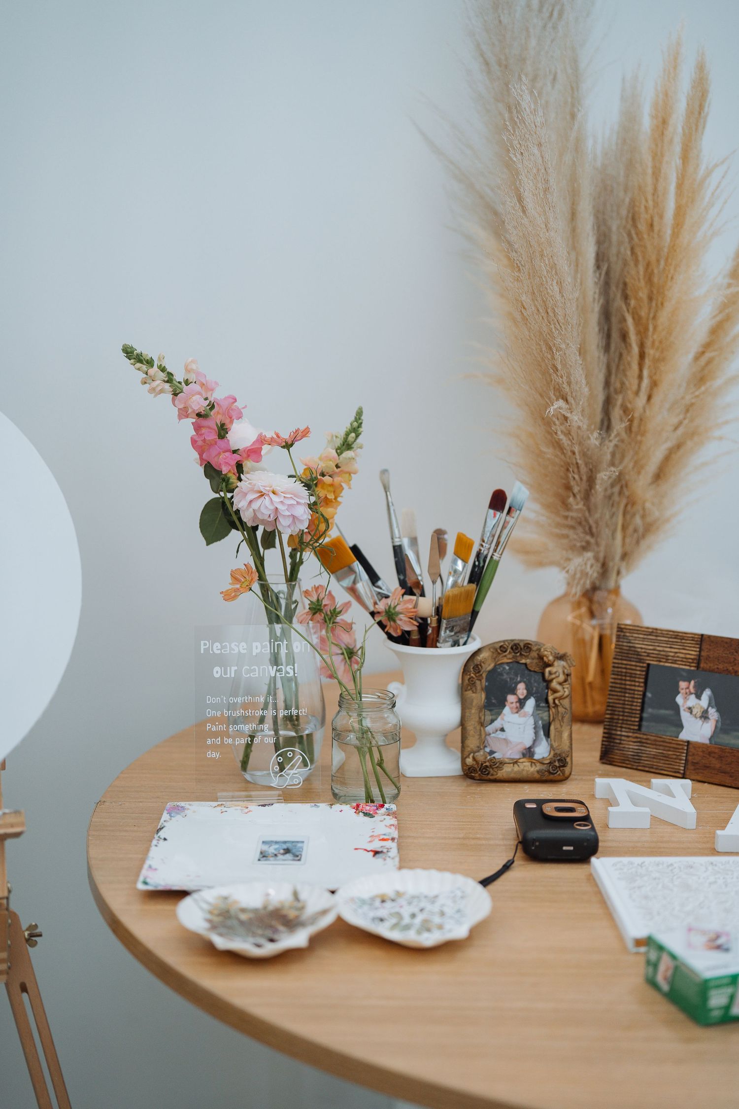 Decorative vanity setup with pampas grass, flowers, and makeup brushes on wooden table.