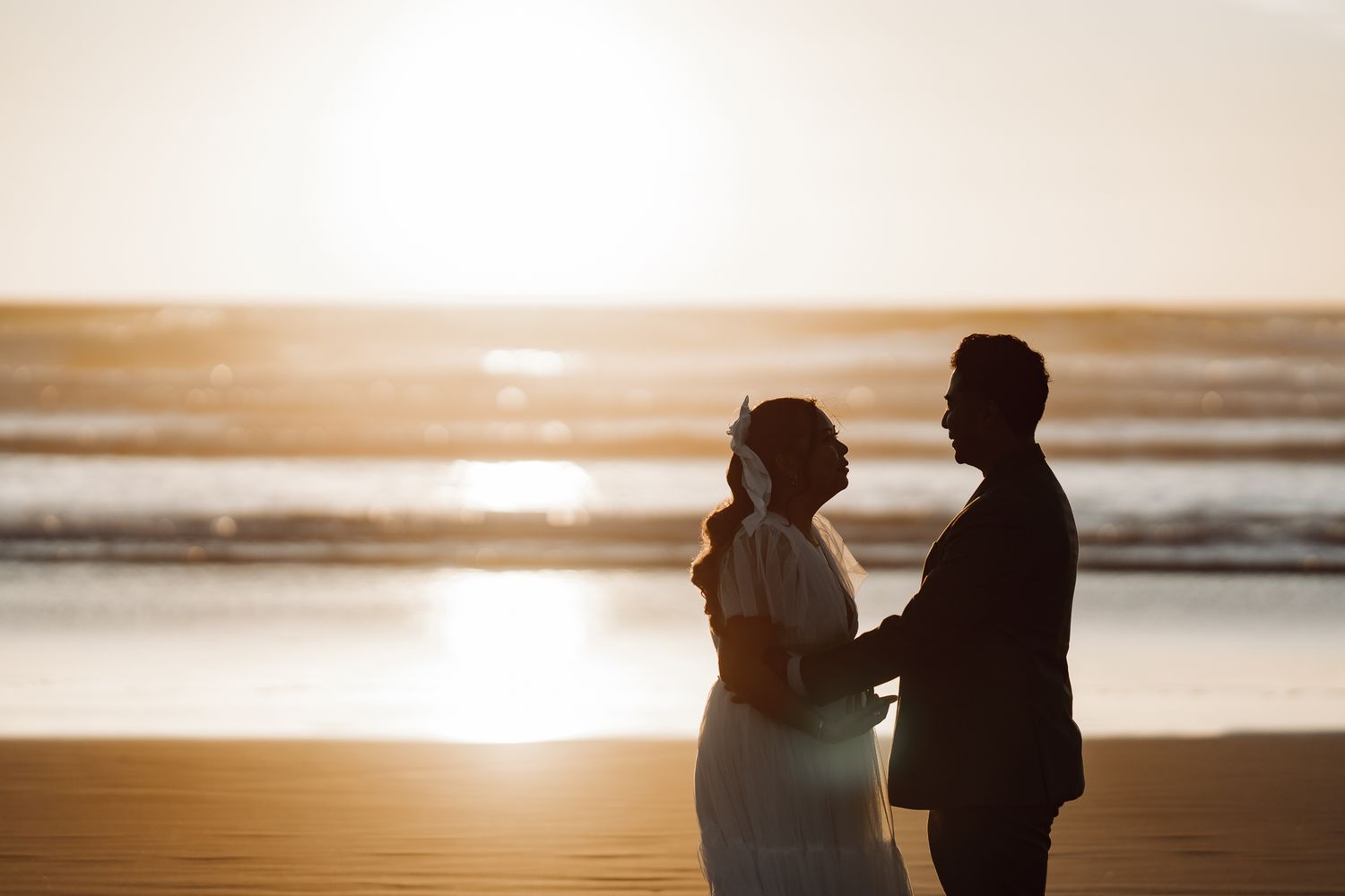 Romantic silhouette of couple on beach during golden hour sunset.