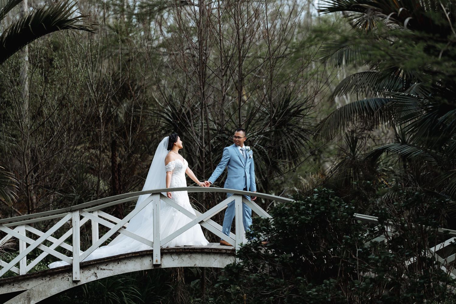 Couple walking across a white wooden bridge in a natural setting.