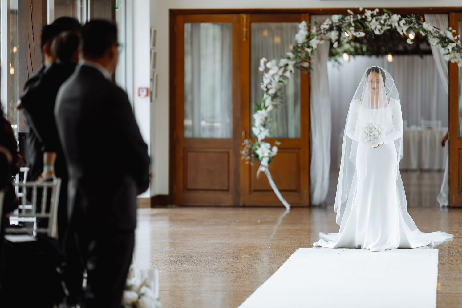 Wedding ceremony setup with bride in flowing veil standing at end of white aisle.