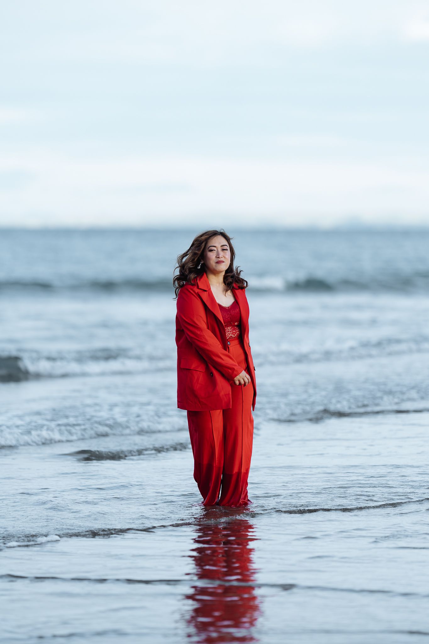 Person wearing bright red outfit stands in ocean waves during moody seascape photoshoot.
