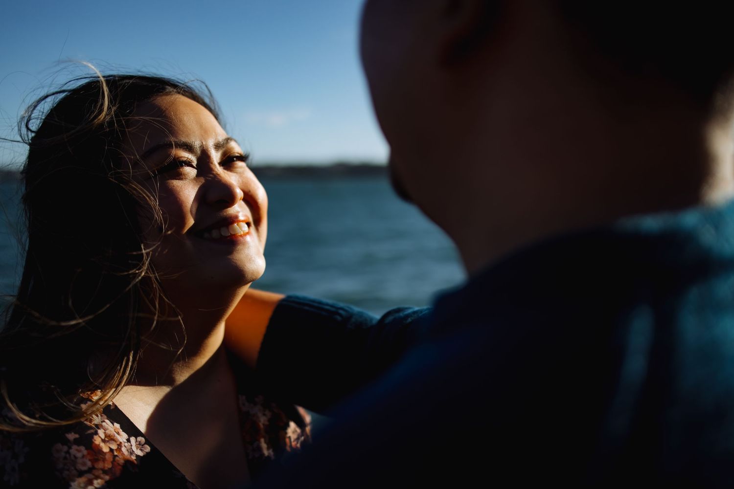 A romantic moment captured by the ocean at sunset with wind-swept hair and warm lighting.