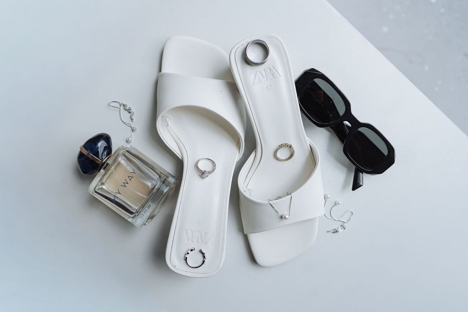 Wedding accessories including rings, jewelry and small decorative items arranged on white surface.
